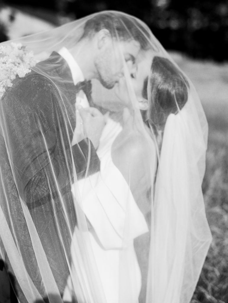 Bride and Groom kiss under veil next to Sea Ranch Lodge 