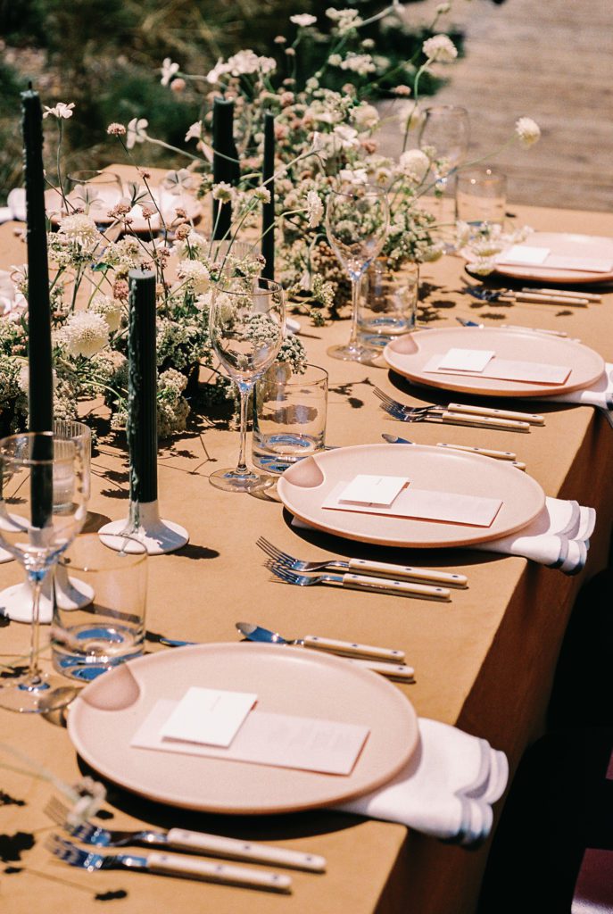Wedding table setting with rust tablecloth and peach dishes next to floral centerpieces